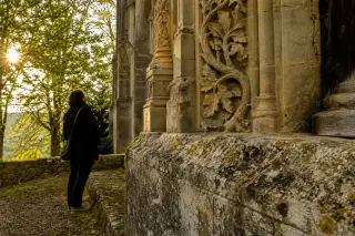 Silhouette observant de près les sculptures végétales sur la façade patinée d’une église gothique méconnue au soleil doré, atmosphère intimiste et contemplative.